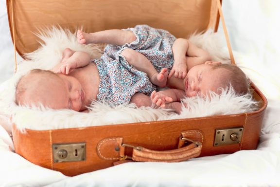 Two newborn babies sleeping peacefully in a vintage suitcase lined with soft fur.