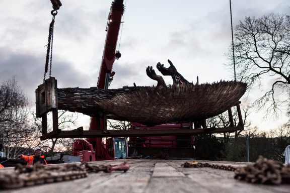 A large, weathered boat being lifted by a crane at a construction site.