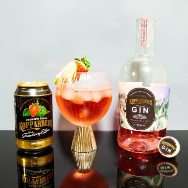 A cocktail with fruit garnish, a can of soda, and a bottle of gin on a reflective surface.