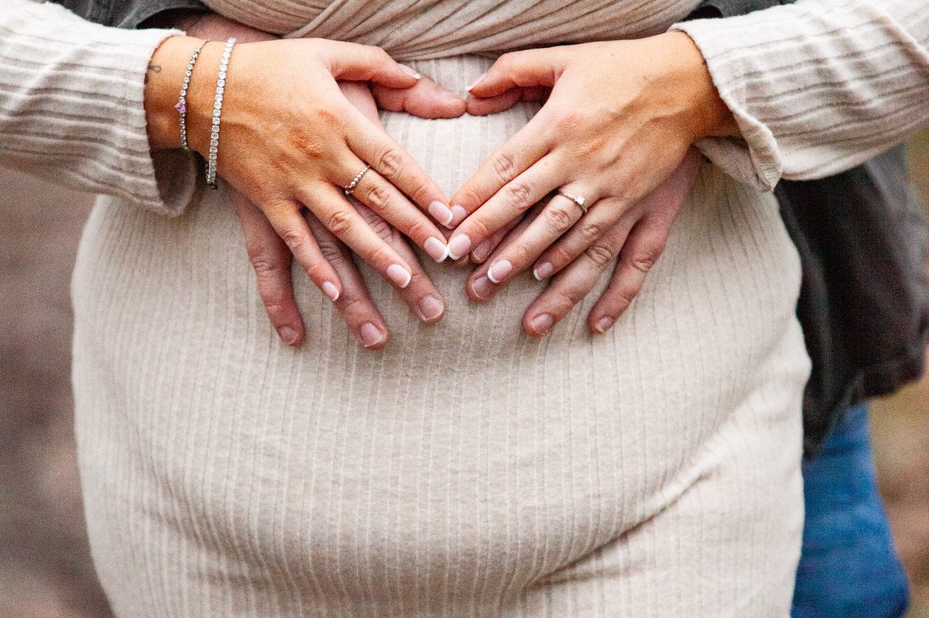 Two hands forming a heart shape over a pregnant belly.