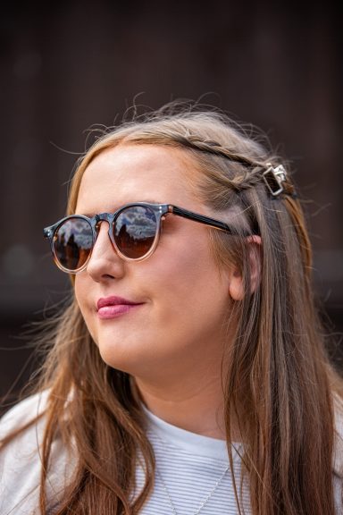 Young woman with long hair wearing sunglasses and a white t-shirt, smiling softly.