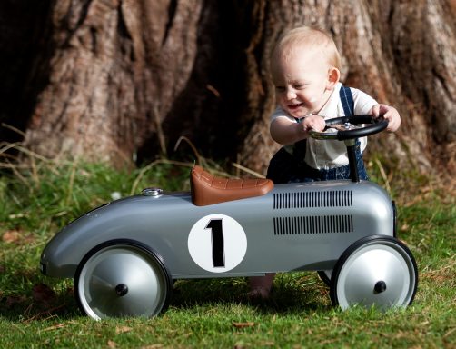 A young child happily plays with a small silver toy car outdoors.