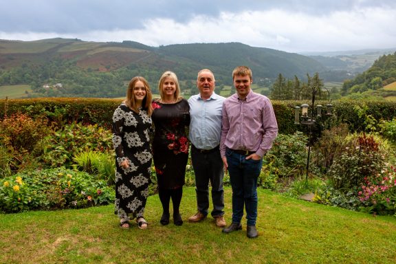A family of four people posing in a picturesque garden with mountains in the background.