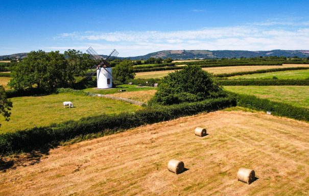 Scenic view of fields with hay bales, a windmill, and distant hills under a clear blue sky.