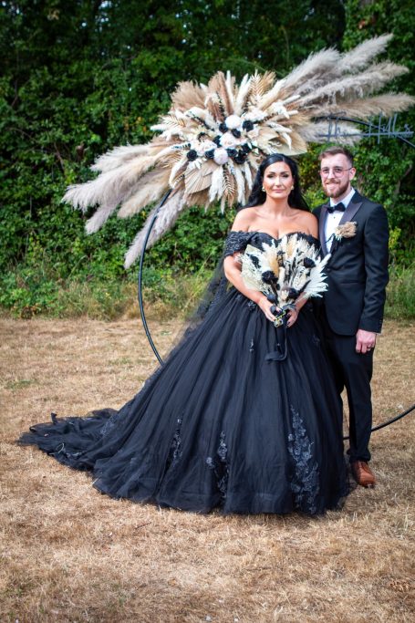 A couple in elegant attire, with the woman in a striking black gown and dramatic feather arrangement.