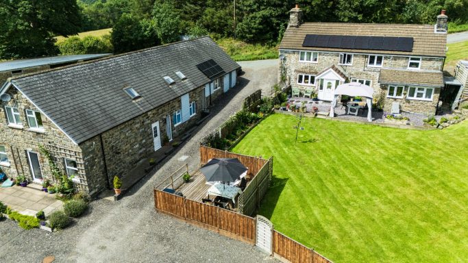Aerial view of two stone buildings, one with solar panels, set in a green lawn.