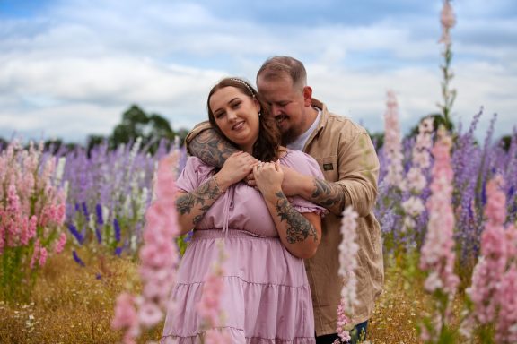 Couple embracing in a field of colourful flowers under a blue sky.