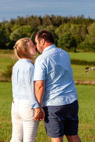 Couple holding hands and kissing in a green field under a blue sky.