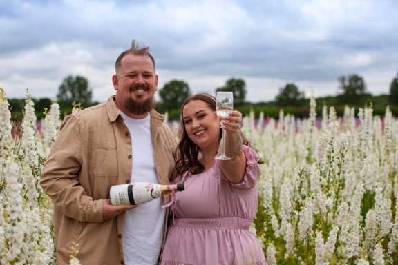 A couple celebrating with champagne in a field of white flowers.