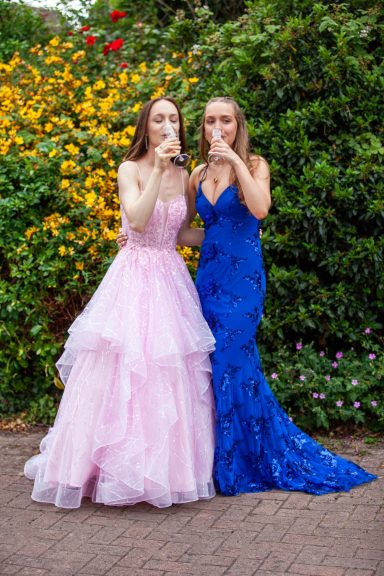 Two women in elegant gowns, one pink and one blue, posing together in a floral garden.