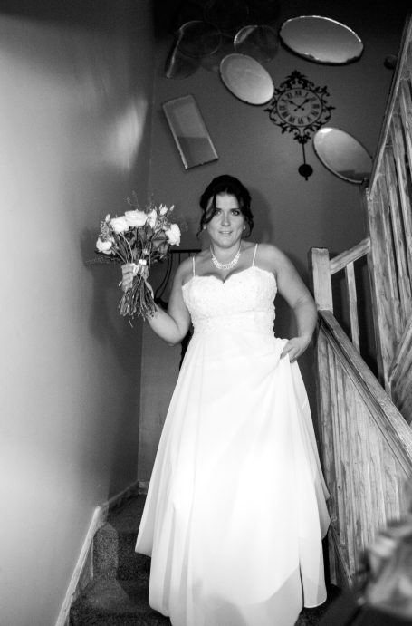 Bride descending a staircase, holding a bouquet of roses, wearing a white gown.