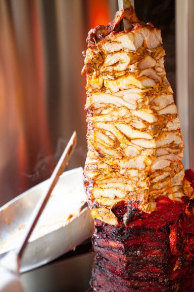 A vertical stack of marinated grilled chicken kebab meat, being sliced ready to serve