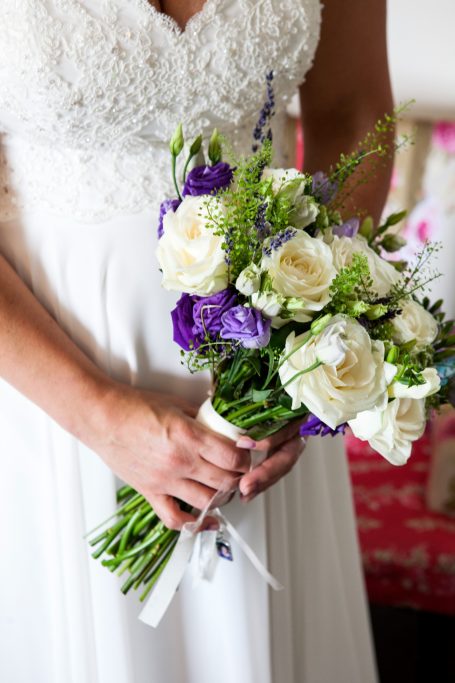 A bride holding a bouquet of white and purple flowers.