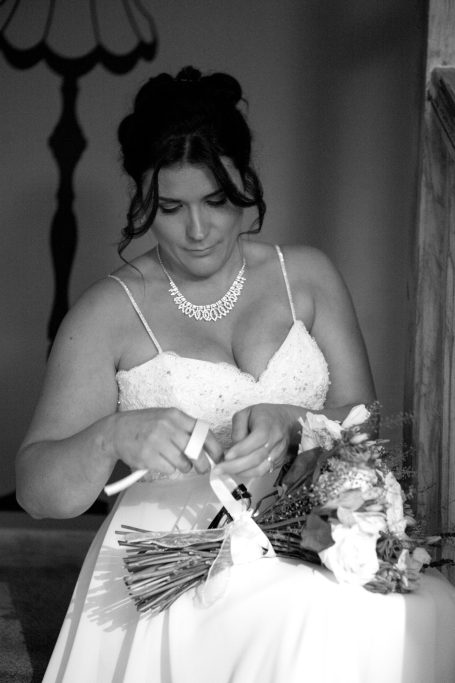 Bride in a white gown adjusting her bouquet with a thoughtful expression.