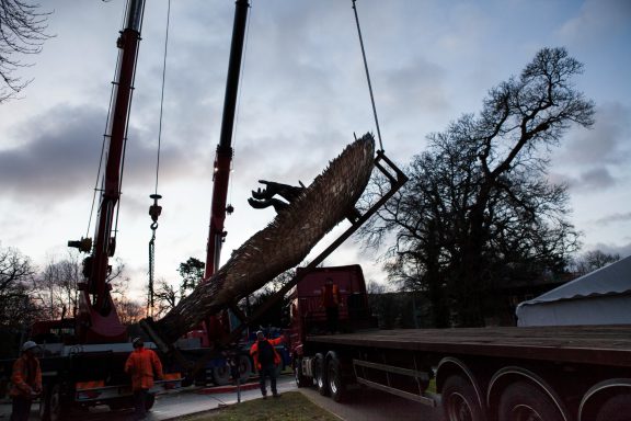 Heavy machinery lifting a large log during sunset, with workers nearby.