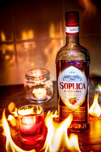 A bottle of Soplica vodka with a lit candle and flames in the foreground.