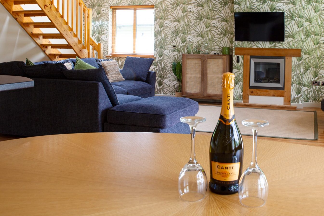 Champagne bottle with glasses set on a table, modern living room in the background.