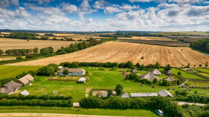 Aerial view of farmland with fields, houses, and a blue sky with scattered clouds.