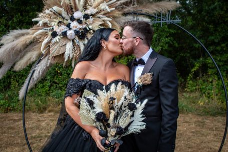 Couple kissing, surrounded by a decorative floral arrangement in a natural setting.