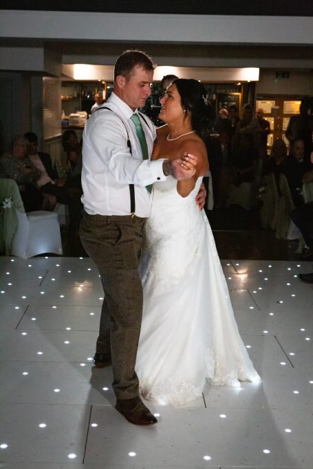A couple dances romantically on a light-up floor at their wedding reception.