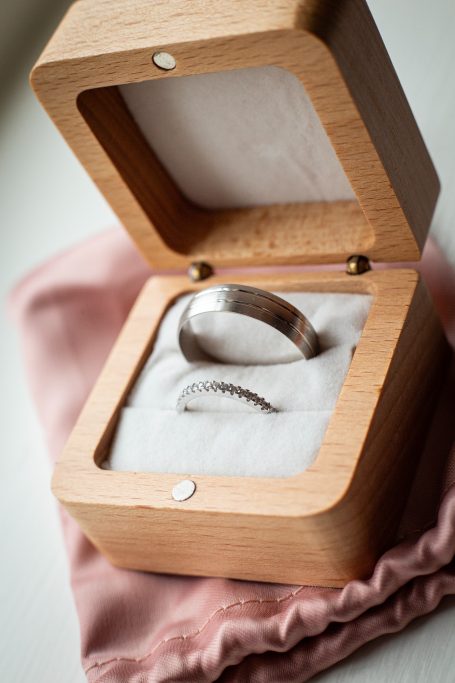 Two silver wedding rings nestled in a wooden ring box on a soft fabric surface.