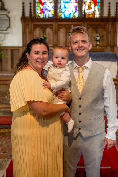 A smiling family posing together in a church, with a child held by the mother.