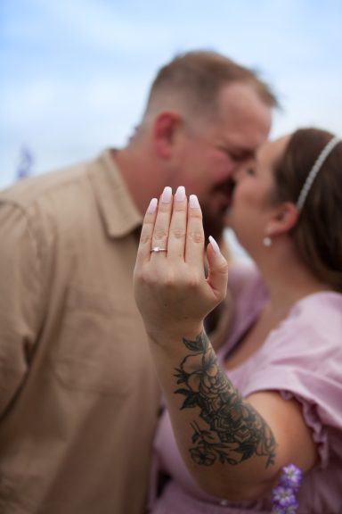 Couple kissing, woman showing a hand with a prominent ring and tattoo.