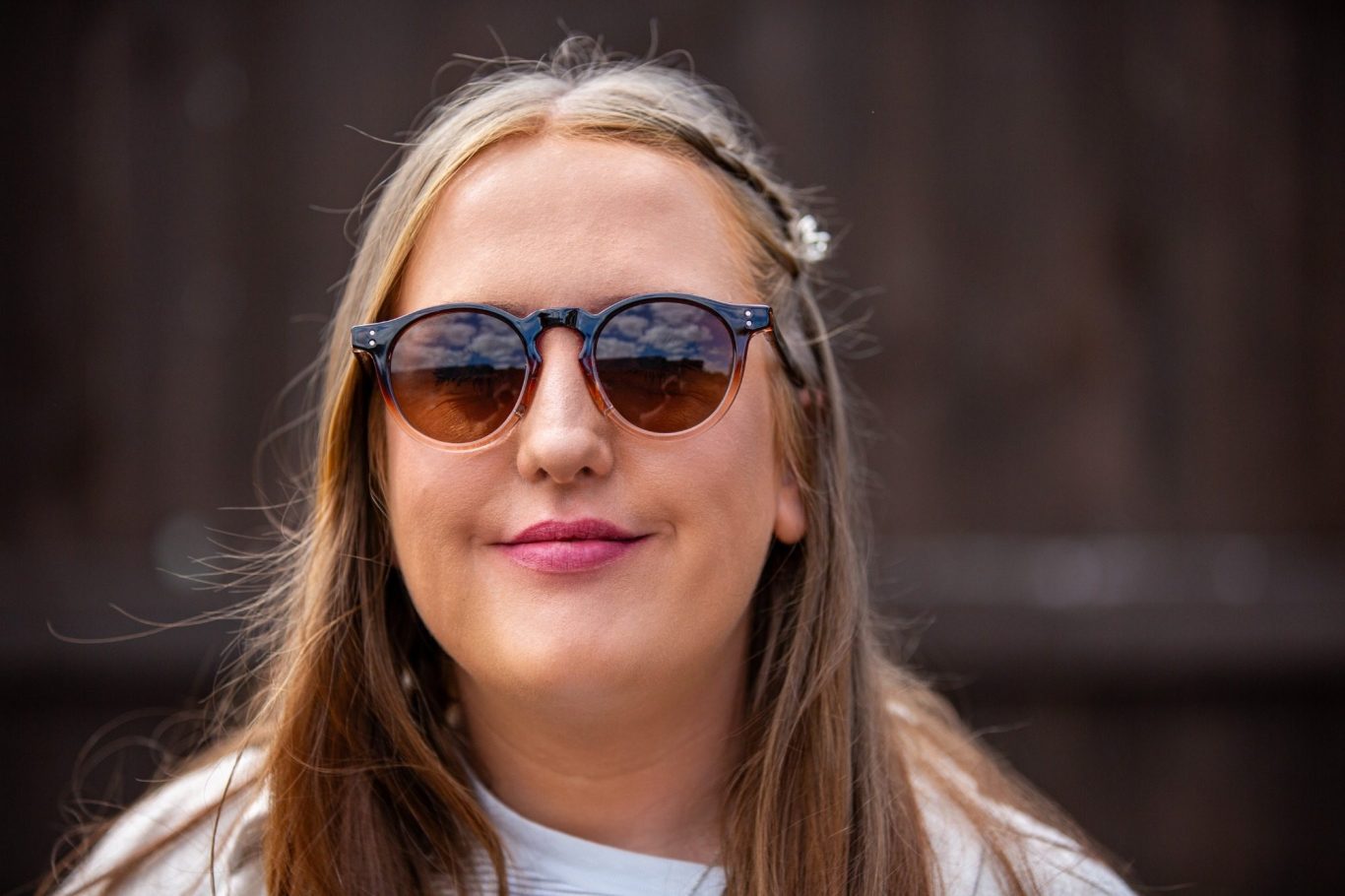 Young woman wearing sunglasses and a light-coloured top, smiling outdoors.