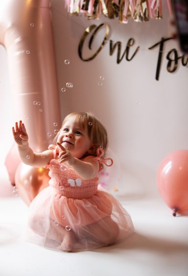 Toddler in a pink dress playing with bubbles at a birthday celebration.