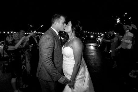 Couple sharing a kiss at a wedding celebration in a romantic evening setting.