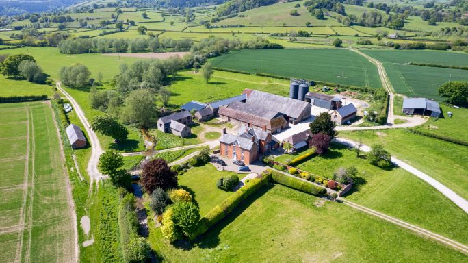 Aerial view of a farm surrounded by green fields and trees.