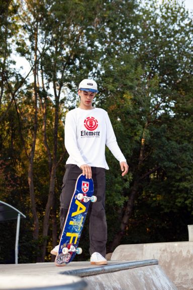 Skateboarder in a white long-sleeve shirt poses with a colourful skateboard.