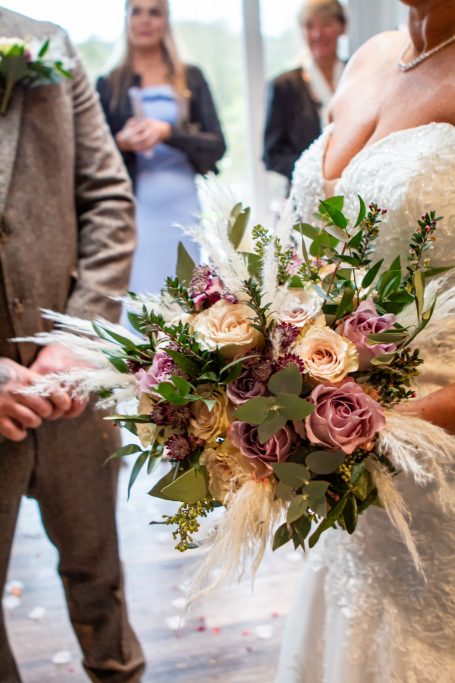 Bride holding a bouquet of roses and greenery during a wedding ceremony.