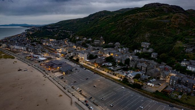A scenic coastline at dusk, featuring a beach and illuminated seaside town along the shore.