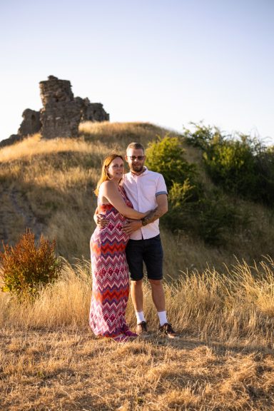 Couple embracing in a scenic outdoor setting with a rocky hill in the background.