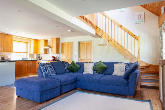 Bright living room featuring a blue corner sofa and a wooden staircase.