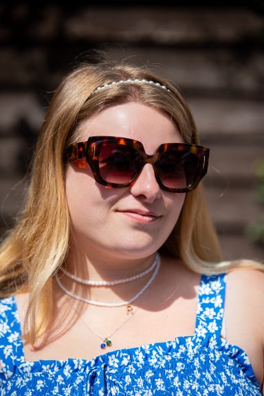 Young woman with long blonde hair, wearing oversized sunglasses and a blue floral top.