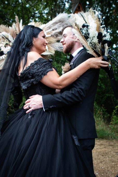 A couple embraces in a forest, dressed in elegant wedding attire, with dramatic decor.