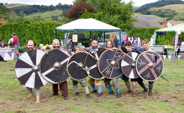 Group of six people in historical costumes holding shields at an outdoor event.
