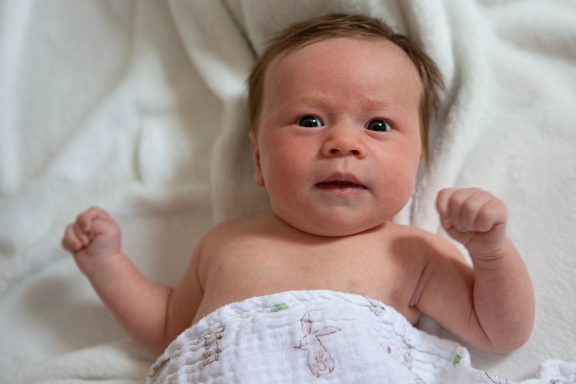 Newborn baby with short hair lying on a soft blanket, looking attentively.