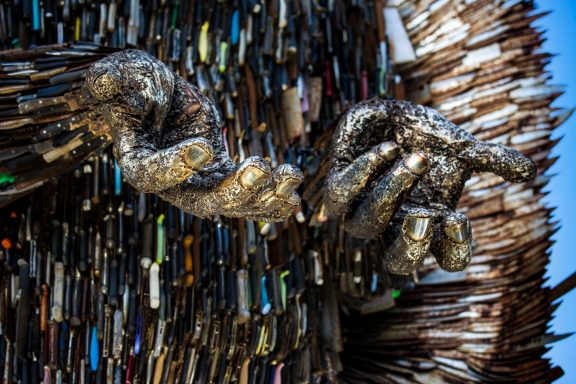A close-up of a sculpted hand made of metallic materials, surrounded by mixed materials.