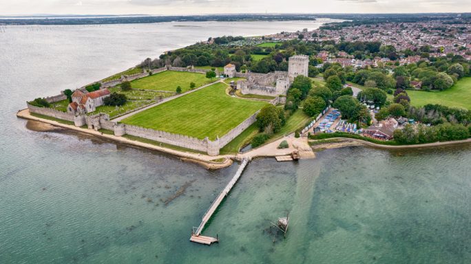 Aerial view of a coastal area with green fields, buildings, and a small pier.