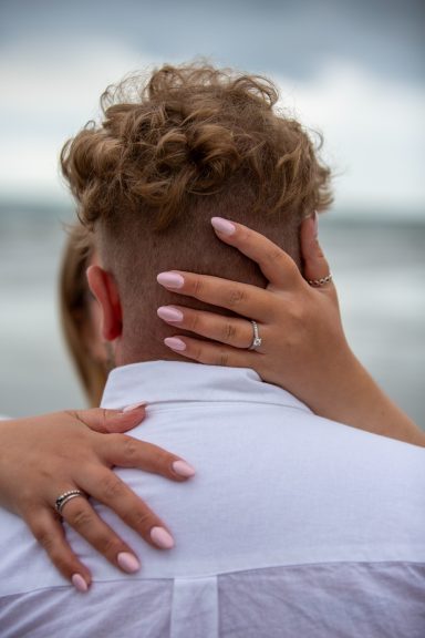 Couple embracing at the beach, with one partner's hand on the other's head.