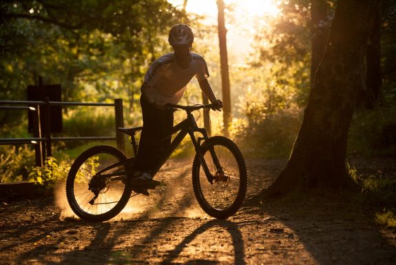 A cyclist performing a trick in a sunlit forest setting.