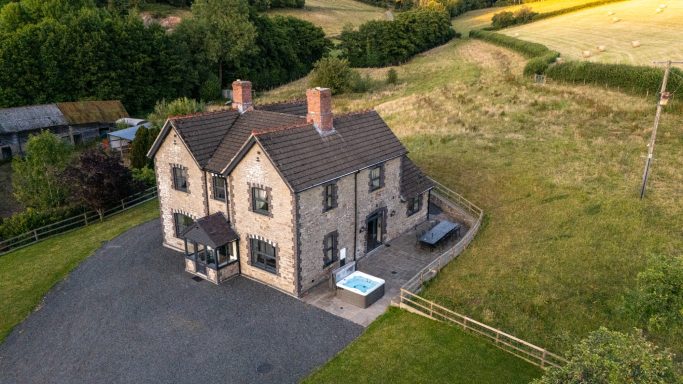 Aerial view of a large house surrounded by green fields and trees.