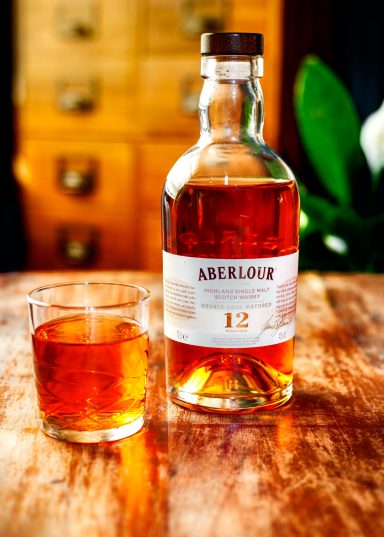 A bottle of Aberlour 12 whisky with a glass filled beside it on a wooden surface.