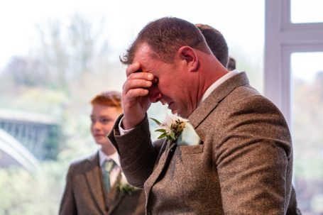 A man in a suit wipes his forehead, appearing emotional, with two younger boys in the background.