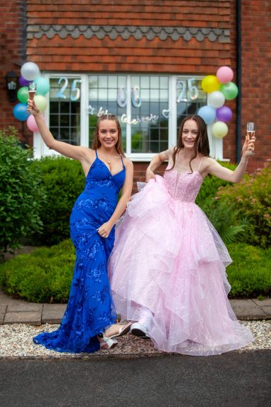 Two young women in formal dresses, one blue and one pink, posing with balloons in a garden.