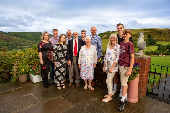 A family of twelve people posing outdoors with a scenic landscape in the background.