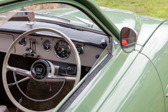 Interior of a vintage green car, featuring a classic steering wheel and dashboard.